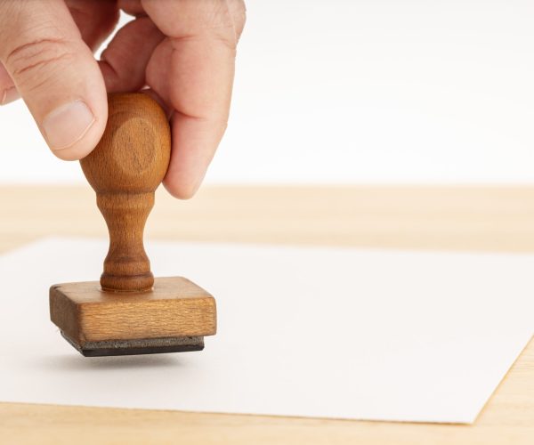 Hand holding a Rubber stamp and blank paper on wooden table. White background. Copy space